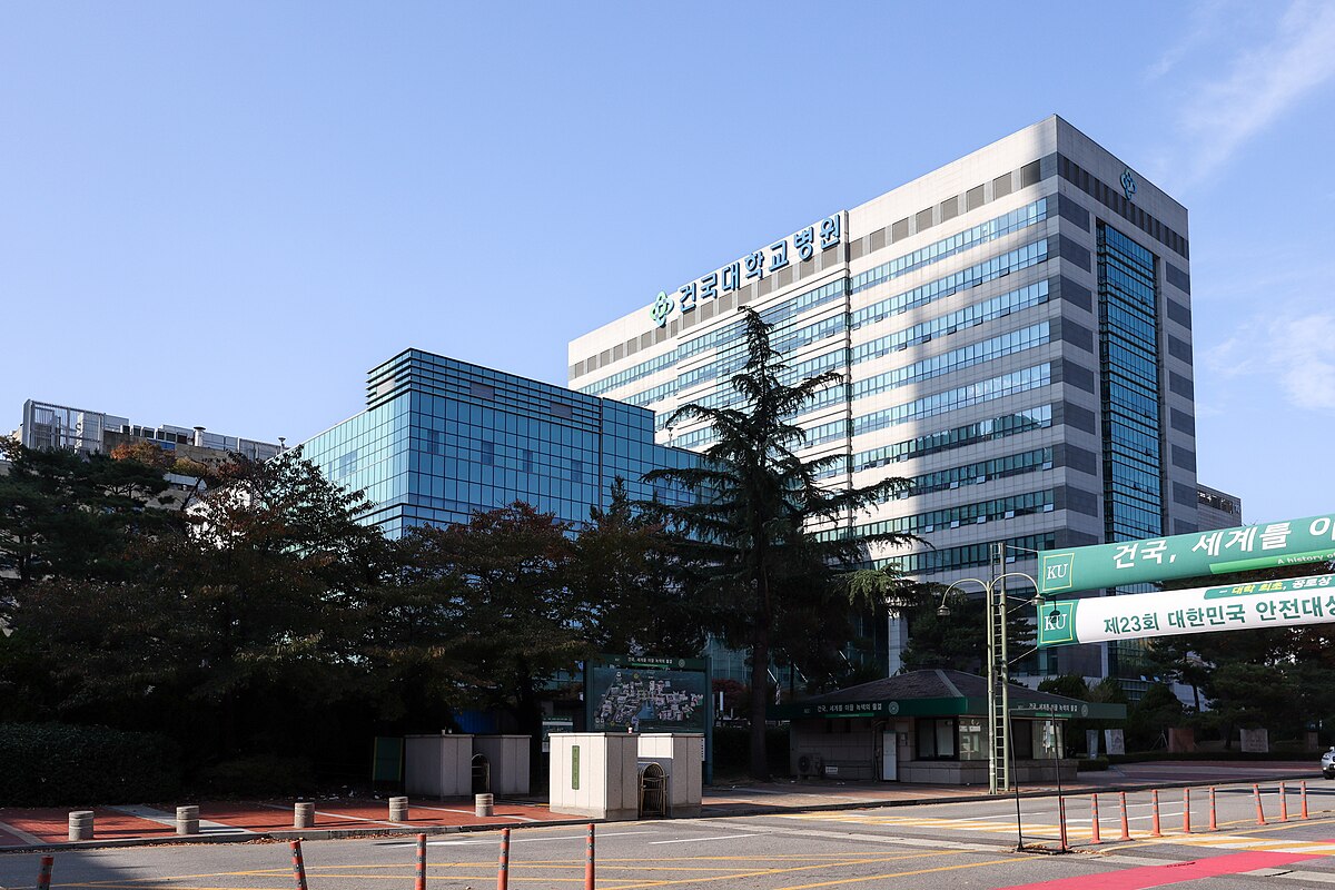 Modern hospital with glass facade under blue sky, trees and quiet street around.