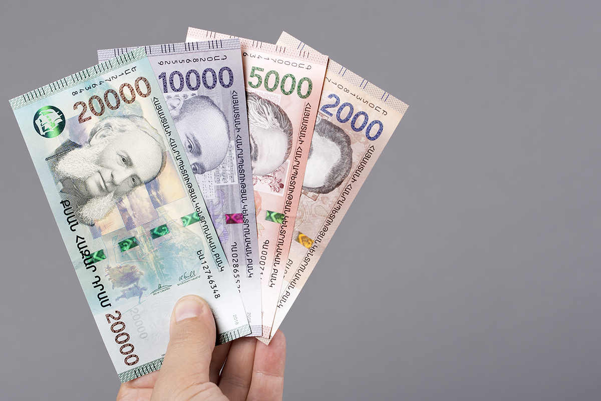 Hand holding colorful Armenian banknotes: 2,000 to 20,000 drams on gray background