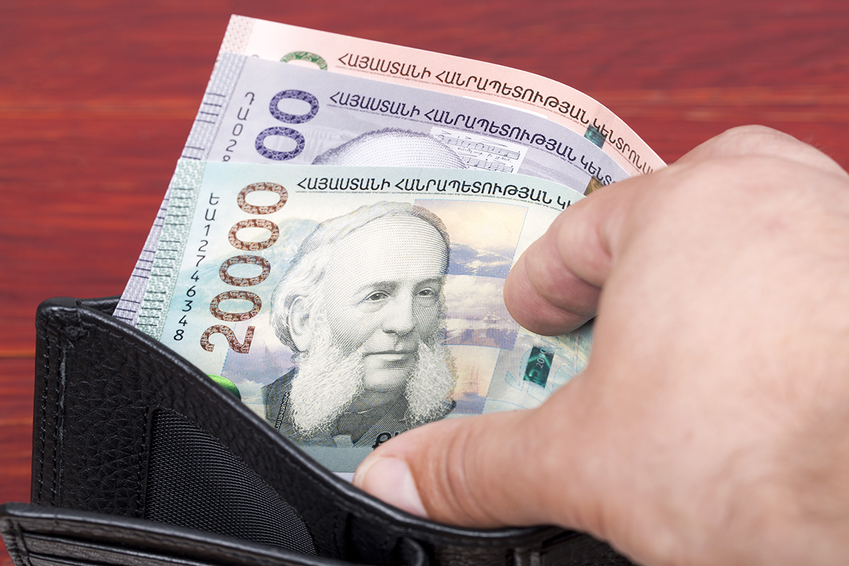 Hand holding open black wallet with Armenian banknotes on wooden background, designs visible