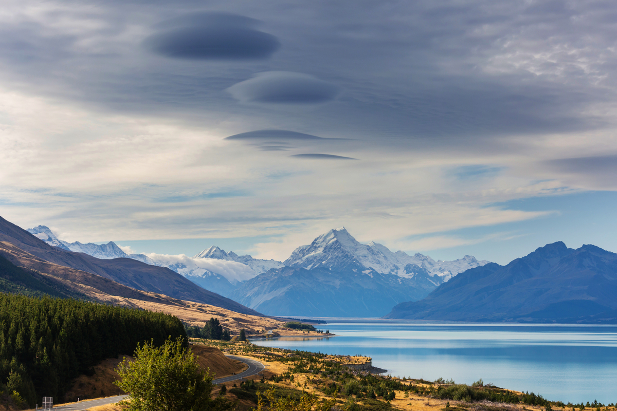 Serene lake reflecting snow-capped mountains under unique, tranquil cloud formations.